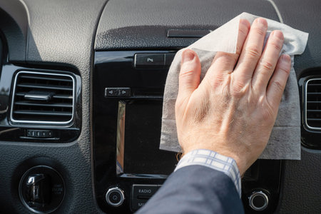 Middle age businessman in a blue suit cleaning front dashboard of a car using antivirus...