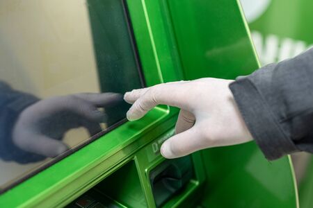 Men hand in protective rubber gloves touches the screen of an ATM during coronavirus epidemic. Pandemic.の写真素材