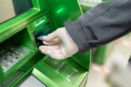 Men hand in protective rubber gloves putting credit card at ATM against coronavirus. Pandemic.の写真素材