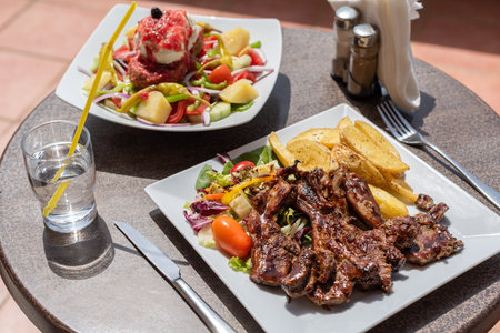 Lunch on the plate with lamb, potato and salad on the table outside on the balcony. Spring or summer blooming trees and flowers in the garden.の写真素材