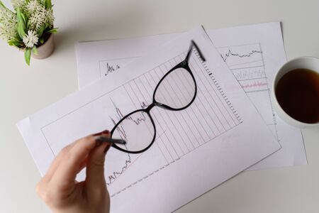 Top view. Business woman sitting at table with glasses, cup of coffee and working  with graphics and charts printed on the paper.の写真素材