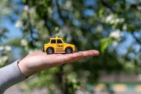The hand of man holding a yellow toy taxi car on the background of blooming sakura. Ecology car. Concept. Taxi city service. Spring time.の写真素材