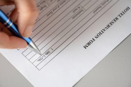 Woman filling hotel reservation form putting check mark on Mrs. Reception desk. Hotel service, registration. Close up. Selective focus.の写真素材