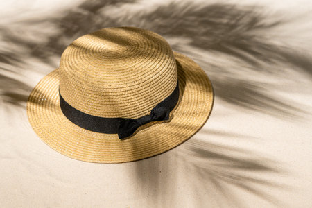 Summer straw hat on sand through the branches of palm and shadow palm tree. Travel, holiday,...