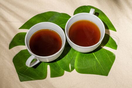 Cup of tea on sand of tropical beach under palm tree branches shadow. Bali, travelの写真素材