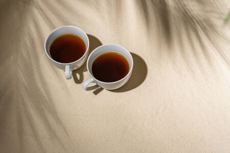 Cup coffee on sand of tropical beach under palm tree  branches shadow. の写真素材
