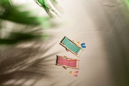 Aerial view two deck chair, glass of juice, flip flops on sand through the branches of palm and shadow palm tree. Travel, holiday, summertime, romantic concept. Top view.の写真素材