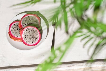 Dragon fruit, pitaya on a white wooden tray on the sand of tropical beach under a palm tree. Exotic food, snack. Summer travelの写真素材