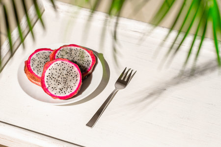 Dragon fruit, pitaya on a white wooden tray on the sand of tropical beach under a palm tree. Exotic...