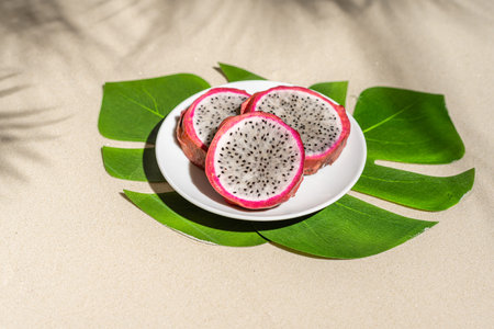Dragon fruit, pitaya on palm tree leaves on the sand of tropical beach. Exotic food, snack. Summer...