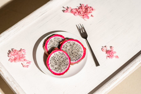 Dragon fruit, pitaya on a white wooden tray on the sand of tropical beach under a palm tree. Exotic...