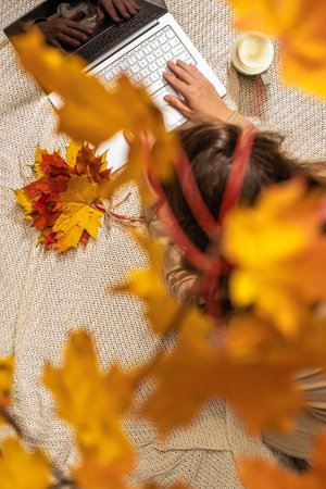 Autumn. Woman freelancer on the plaid with laptop, cup of coffee under branch of golden maple leaf...