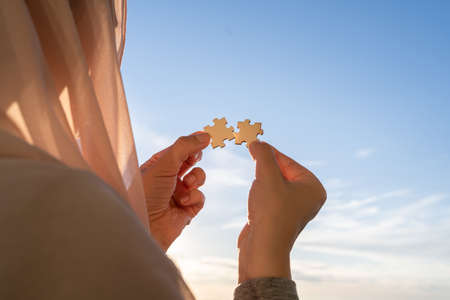 Two pieces of a puzzle in muslim women hands on sunset blue sky background. Man and woman. relationship concept. Travel, vacationの写真素材