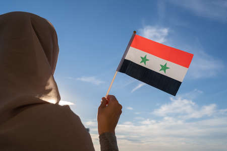 Silhouette of muslim woman in head scarf with Syria flag at blue sunset sky. Concept of freedomの写真素材
