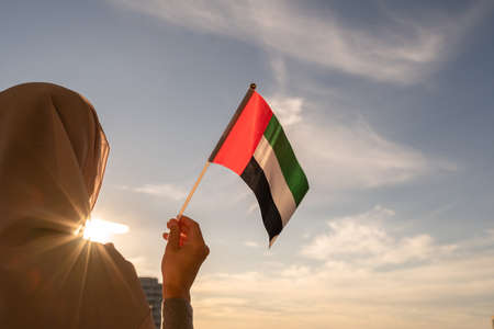 Silhouette of muslim woman in head scarf with United Arab Emirates flag at blue sunset sky. Concept of freedomの写真素材