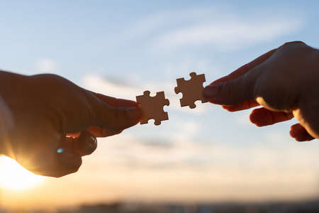 Two pieces of a puzzle in women hands on sunset blue sky background. Man and woman. relationship concept. Travel, vacationの写真素材