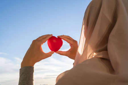 Silhouette of muslim woman in head scarf with red heart on blue sunset sky background. Conceptの写真素材
