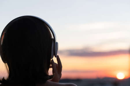 Back view silhouette of relaxed woman wearing headphones meditating listening to music on the beach at sunsetの写真素材