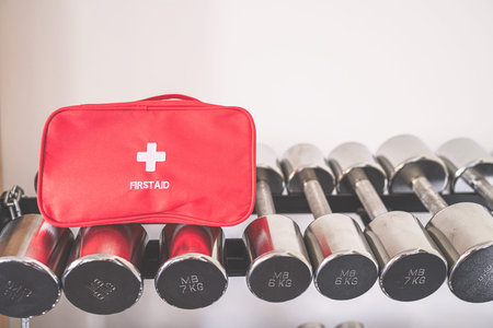 First aid kit red box on iron dumbbells in the fitness gym opposite the sport equipment and jogging...