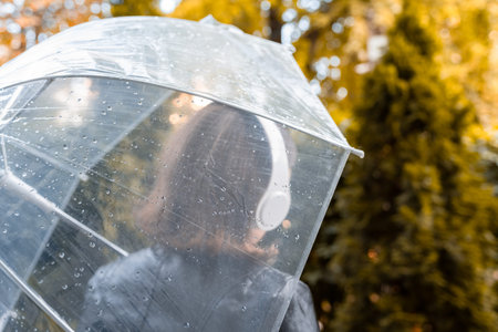 Autumn. Lonely sad woman in a headphones walking in a park, garden. View through wet transparent...