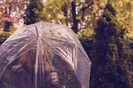 Autumn. Lonely redhead girl under a transparent umbrella with rain drops walking in a park, garden....