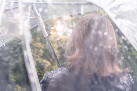 Autumn. Lonely sad redhead woman walking in a park, garden. View through wet transparent umbrella...