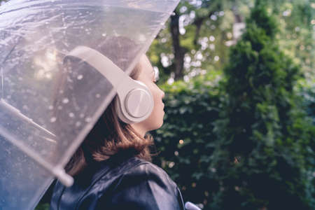 Autumn. Lonely sad woman in a headphones walking in a park, garden. View through wet transparent umbrella with rain drops. Rainy day landscape. Vintage tonedの写真素材