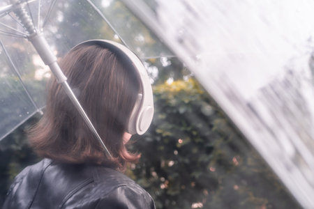 Autumn. Lonely sad woman in a headphones walking in a park, garden. View through wet transparent...
