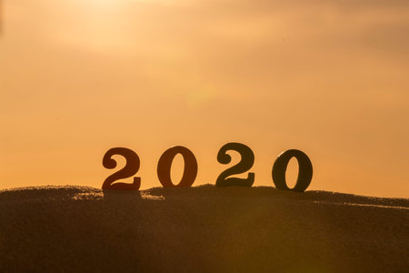 Silhouette of 2020 wooden numbers on the sand on the beach at sunset. Setting sun. The symbol of the...