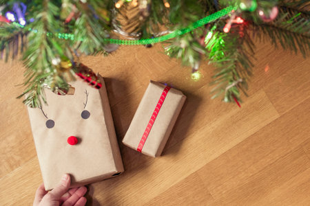 Man putting hand made gift wrapping in a kraft paper under christmas tree. Presents for family. Top...