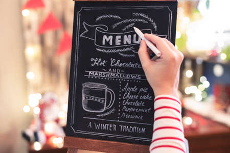 Woman drawing christmas menu of cocoa bar on small chalkboard.の写真素材