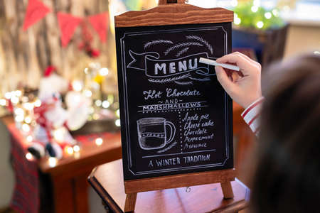 Woman drawing christmas menu of cocoa bar on small chalkboard.の写真素材
