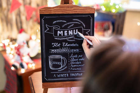 Woman drawing christmas menu of cocoa bar on small chalkboard.の写真素材
