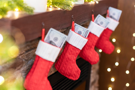 American, US dollars in Christmas red socks for gifts on the fireplace in bokeh lightsの写真素材
