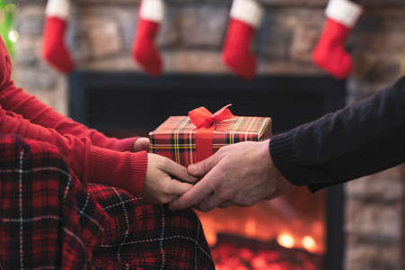 Man giving Christmas and New Year Gift box to woman in front of the fireplace with flame.の写真素材