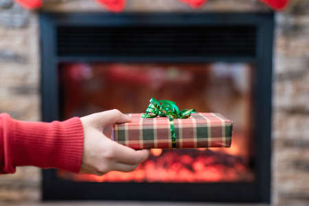 Woman giving Christmas and New Year Gift box to woman in front of fireplace with flame. Xmas concept.の写真素材