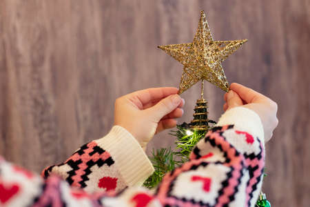 Woman decorating top of christmas tree with star at home. Cropped, close upの写真素材