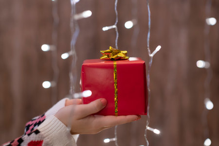 Woman hand holding out gift box through the glowing garland. Christmasの写真素材