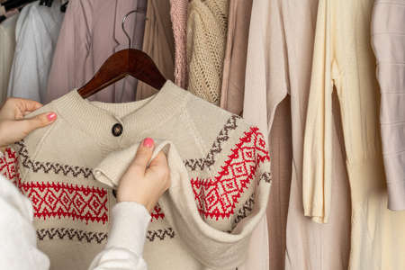 Woman shopper, customer choosing winter pulover with chtistmas ornament from assortment of clothing in garment store. Shopping. Winterの写真素材