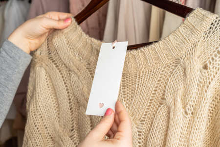 Woman shopper looking on empty tag, template choosing sweater from clothes in garment store. Shopping.の写真素材