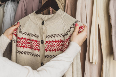 Woman choosing woolen sweater with christmas ornament in home cupboard. Season concept