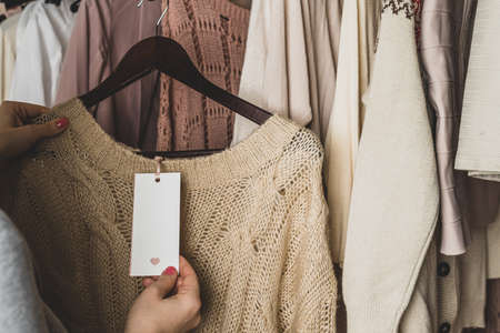 Woman shopper looking on tag choosing sweater from clothes in garment store. Shopping.の写真素材