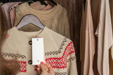 Woman customer looking on tag choosing sweater with christmas ornament in garment store. Shopping. Winterの写真素材