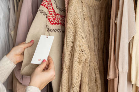 Woman customer looking on tag choosing sweater with christmas ornament in garment store. Shopping. Winterの写真素材