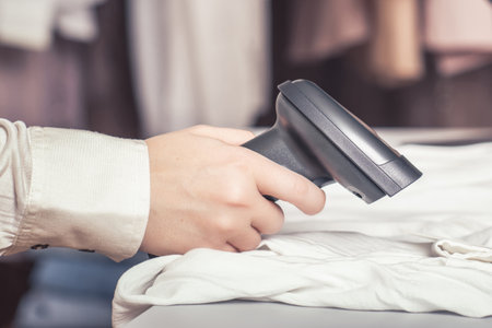 A warehouse woman employee accepts clothes using barcode scanner reading a bar code from price tag of female blouse and adds to the computer base.の写真素材