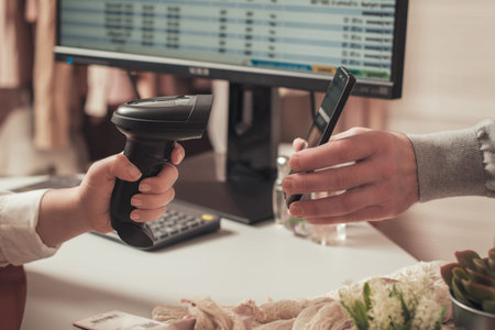 Woman cashier scanning qr code from buyer phone using barcode scanner. Man buying a gift in a female...