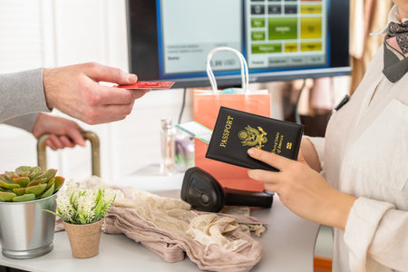 Man holding out american passport with boarding pass to cashier in female boutique store at the airport duty free.の写真素材