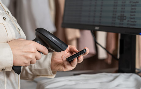 A warehouse woman employee accepts clothes using barcode scanner reading a bar code from phone of...