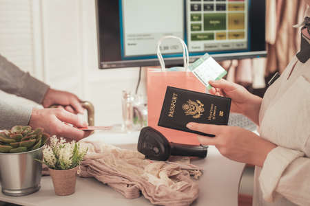 Man holding out american passport with boarding pass to cashier in female boutique store at the airport duty free.の写真素材
