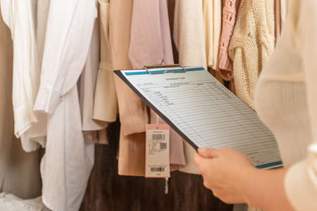 Female entrepreneur holding a clipboard with inventory list while doing inventory in her trendy clothing shopの写真素材